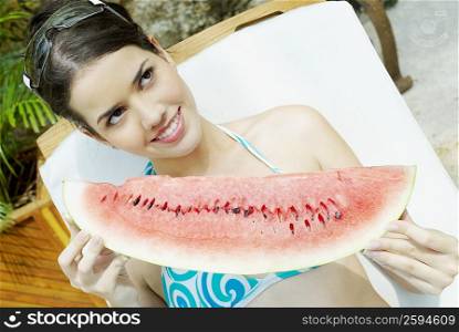 Close-up of a young woman reclining on a chair and holding a slice of watermelon