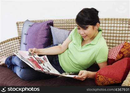 Close-up of a young woman reclining on a couch and reading a newspaper