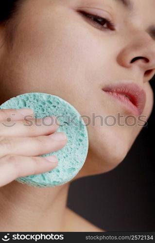 Close-up of a young woman scrubbing her face with a sponge