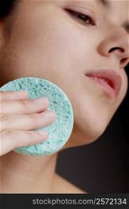 Close-up of a young woman scrubbing her face with a sponge