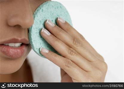Close-up of a young woman scrubbing her face with a sponge
