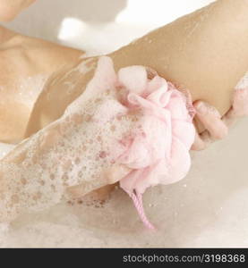 Close-up of a young woman scrubbing her leg with a bath sponge