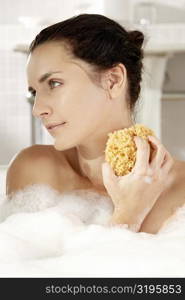 Close-up of a young woman scrubbing her neck with a bath sponge