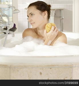 Close-up of a young woman scrubbing her neck with a bath sponge