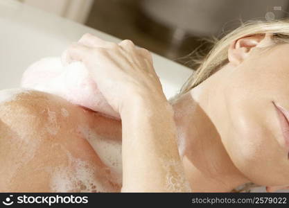 Close-up of a young woman scrubbing her shoulder with a bath sponge