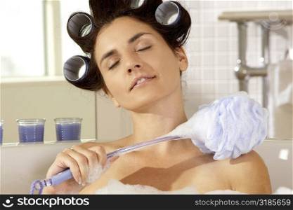 Close-up of a young woman scrubbing her shoulder with a bath sponge