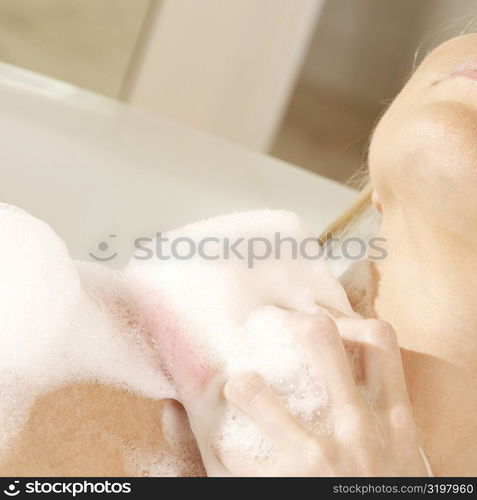 Close-up of a young woman scrubbing her shoulder with a bath sponge