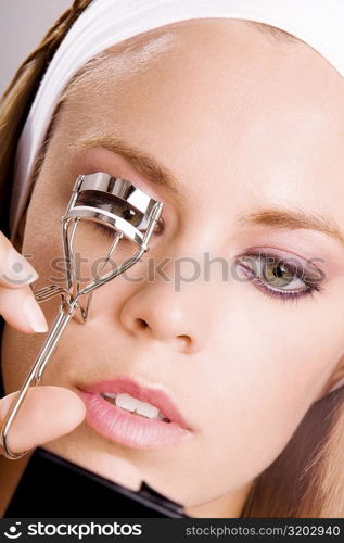 Close-up of a young woman shaping her eyelashes with an eyelash curler