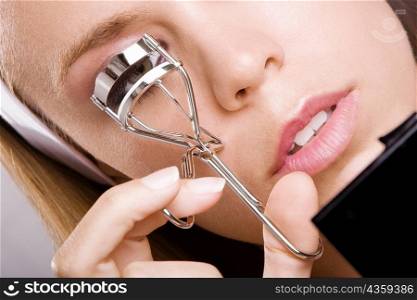 Close-up of a young woman shaping her eyelashes with an eyelash curler