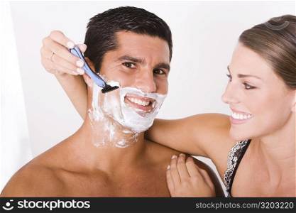 Close-up of a young woman shaving a mid adult man