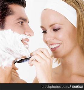 Close-up of a young woman shaving a mid adult man&acute;s face
