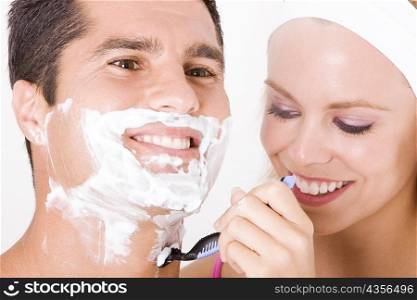 Close-up of a young woman shaving a mid adult man&acute;s face