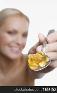 Close-up of a young woman showing vitamin pills in a spoon