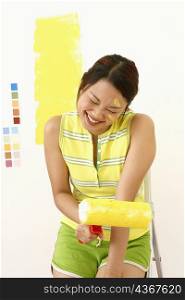 Close-up of a young woman sitting on a ladder and holding a paint roller