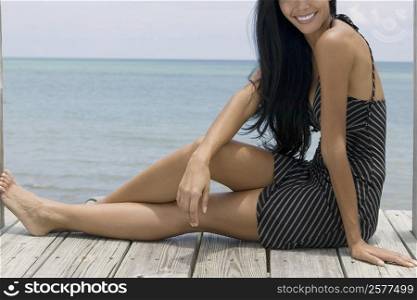 Close-up of a young woman sitting on a pier and smiling
