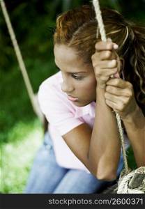 Close-up of a young woman sitting on a swing and looking upset