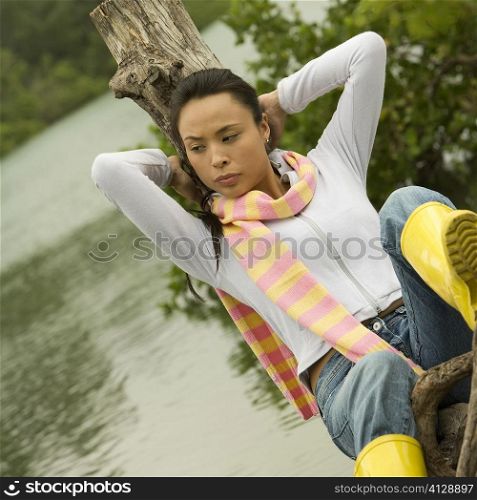 Close-up of a young woman sitting on a tree stump by the lake