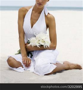 Close-up of a young woman sitting on the beach and holding flowers