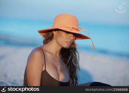 Close-up of a young woman sitting on the beach and wearing a hat