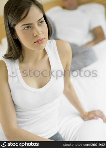 Close-up of a young woman sitting on the bed with a mid adult man in the background