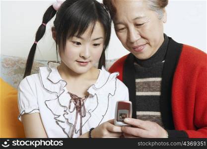 Close-up of a young woman sitting together with her grandmother holding a mobile phone
