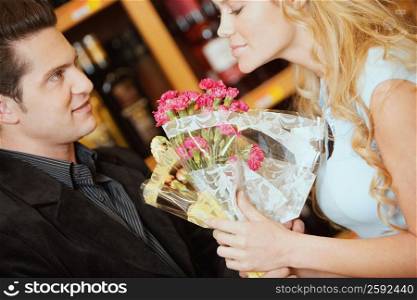 Close-up of a young woman smelling a bouquet of flowers and a young man looking at her