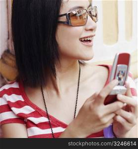 Close-up of a young woman smiling and holding a mobile phone