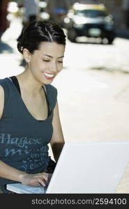 Close-up of a young woman smiling and using a laptop