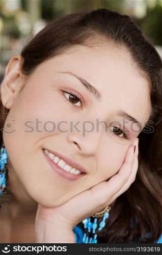Close-up of a young woman smiling with her hand on her chin