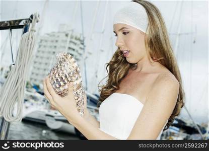 Close-up of a young woman standing on a boat and holding a conch shell