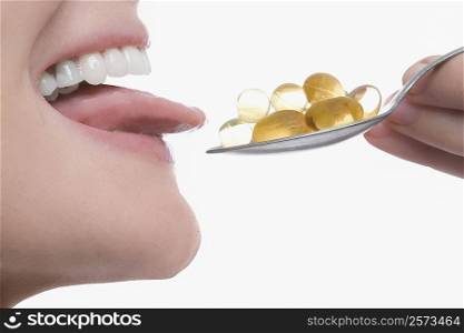 Close-up of a young woman taking a spoonful of pills