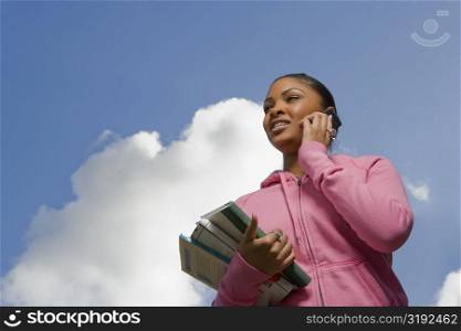 Close-up of a young woman talking on a mobile phone and holding books