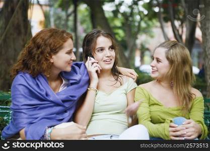 Close-up of a young woman talking on a mobile phone and sitting with her two friends