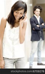 Close-up of a young woman talking on a mobile phone with a young man standing behind her