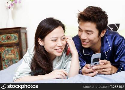 Close-up of a young woman talking on mobile phone with a mid adult man lying beside her