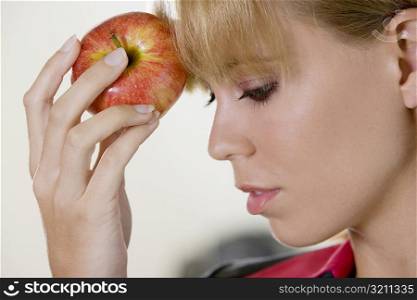 Close-up of a young woman touching an apple against her forehead
