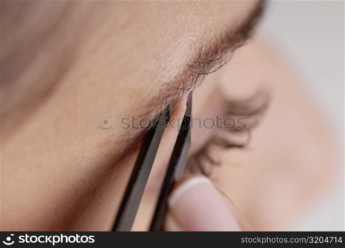 Close-up of a young woman tweezing her eyebrow