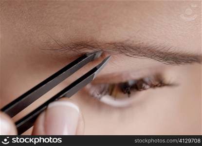 Close-up of a young woman tweezing her eyebrow