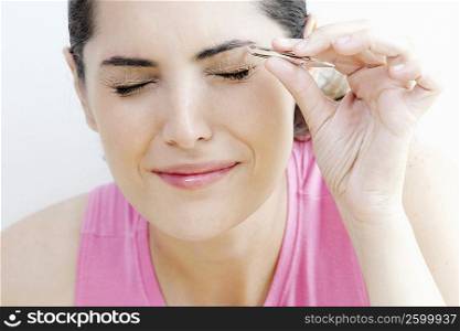 Close-up of a young woman tweezing her eyebrows