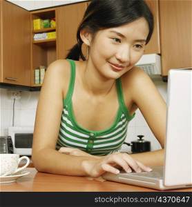 Close-up of a young woman using a laptop at a kitchen counter