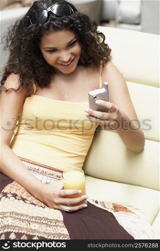 Close-up of a young woman using a mobile phone and holding a glass of orange juice