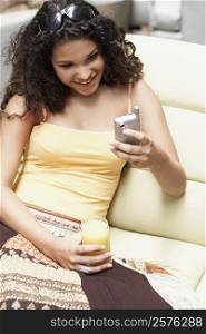 Close-up of a young woman using a mobile phone and holding a glass of orange juice
