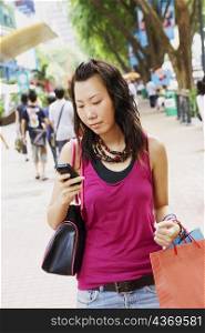 Close-up of a young woman using a mobile phone carrying shopping bags