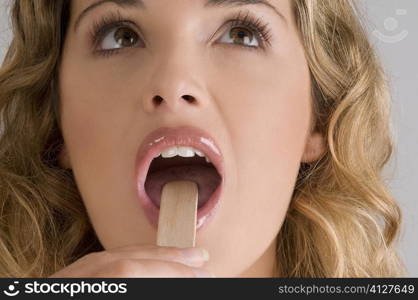 Close-up of a young woman using a tongue depressor to examine her tongue