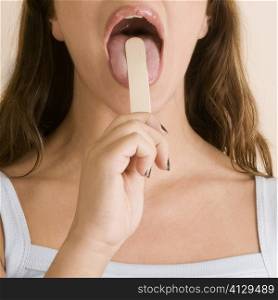 Close-up of a young woman using a tongue depressor to examine her tongue