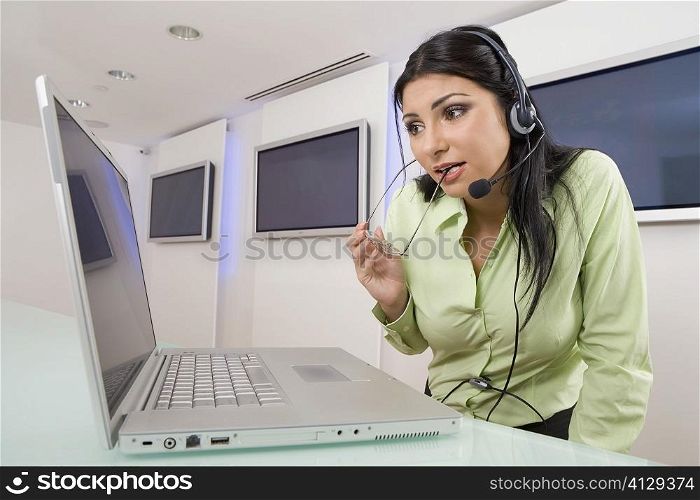 Close-up of a young woman wearing a headset and looking at a laptop