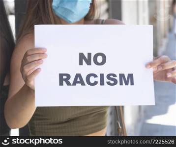Close up of a young woman wearing a surgical mask holding a sign with a message on it on an out of focus background. Safety and awareness concept.. a young woman wearing a surgical mask holding a sign with a message on it. Safety and awareness concept.