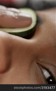 Close-up of a young woman with a cucumber slice on her eye