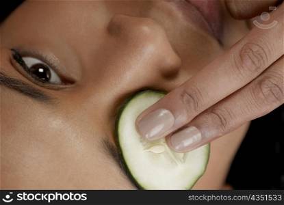 Close-up of a young woman with a cucumber slice on her eye