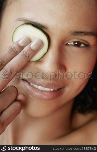 Close-up of a young woman with a cucumber slice on her eye